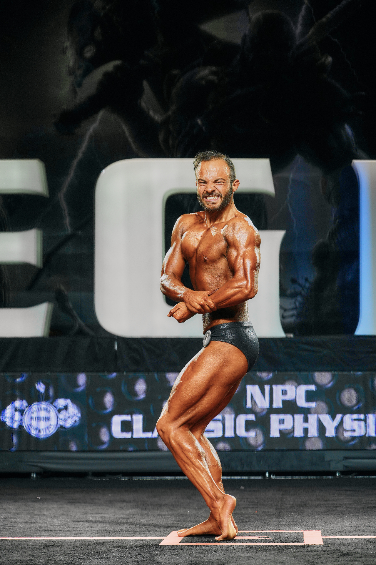 Coach MTS posing on stage at NPC Classic Physique